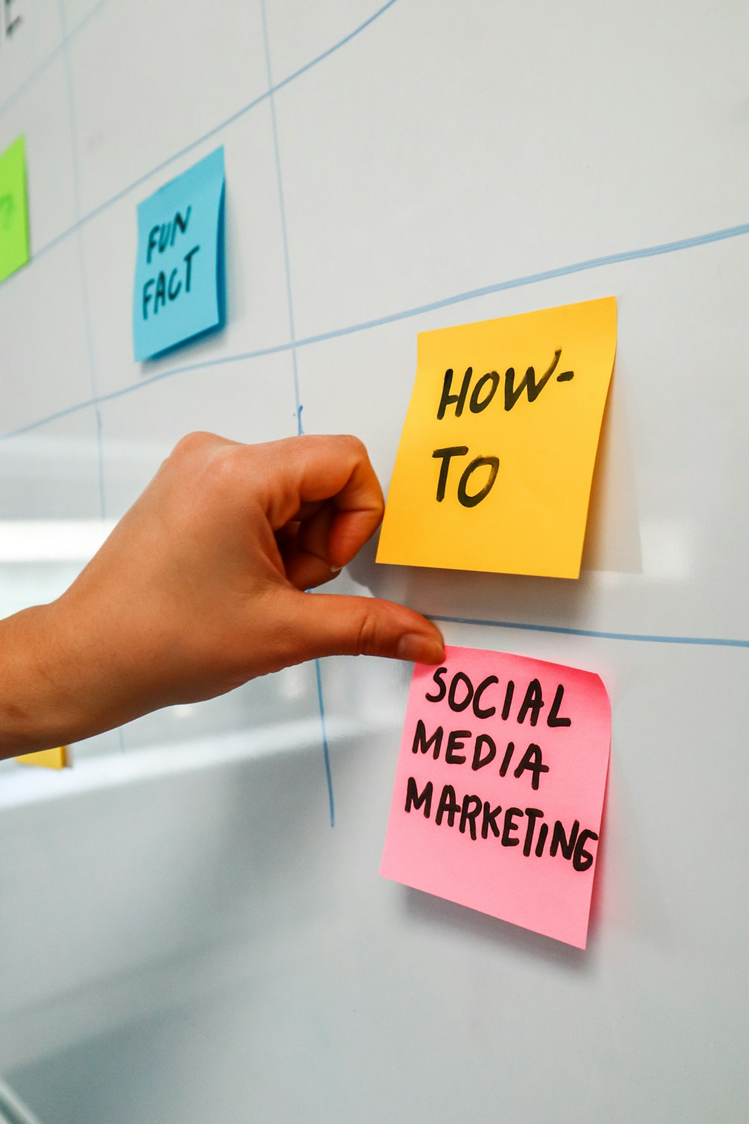 Une personne colle un post-it sur un tableau blanc sur lequel sont écrits les mots Social Media Marketing